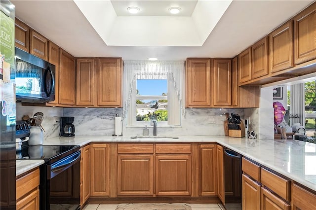 kitchen featuring brown cabinetry, a sink, decorative backsplash, black appliances, and a raised ceiling