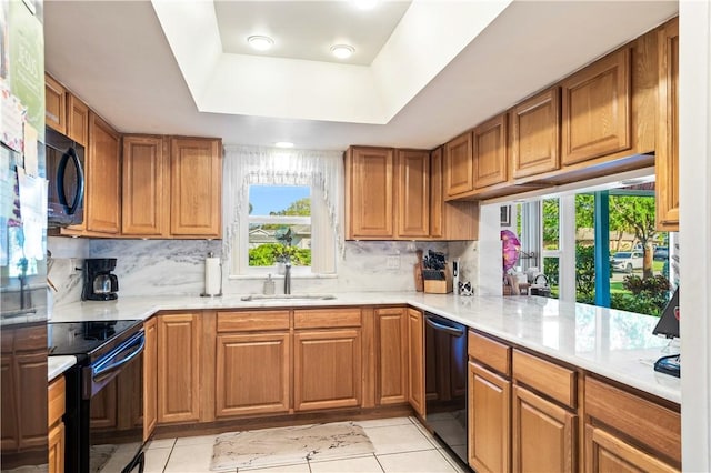 kitchen with light countertops, a tray ceiling, brown cabinetry, black appliances, and a sink