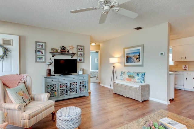 living area with light wood-style floors, visible vents, a textured ceiling, and ceiling fan