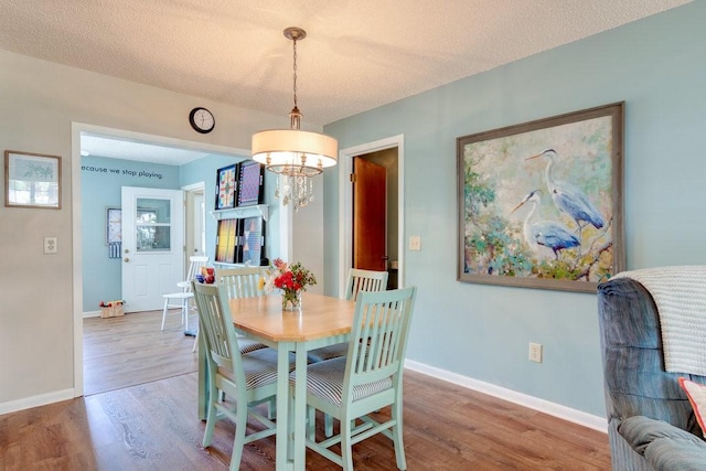 dining space with a textured ceiling, wood finished floors, a notable chandelier, and baseboards