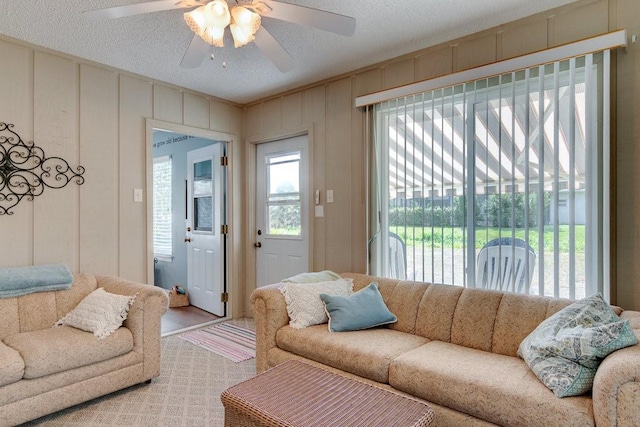living area featuring a decorative wall, a textured ceiling, and ceiling fan
