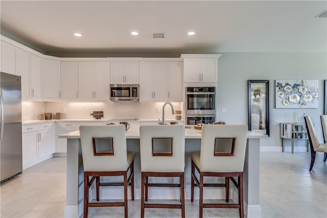 kitchen featuring white cabinetry, appliances with stainless steel finishes, a center island with sink, and a breakfast bar