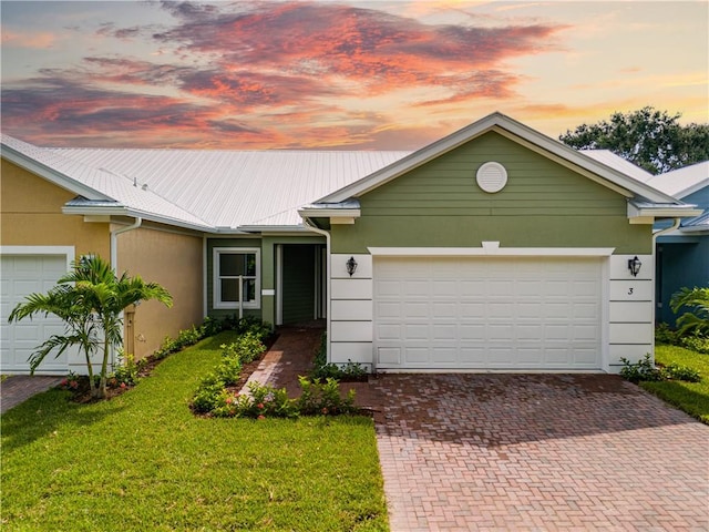 ranch-style home featuring a garage, metal roof, a lawn, and stucco siding