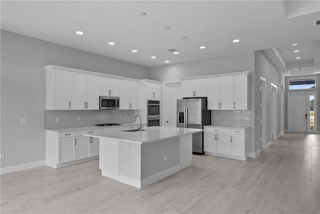 kitchen with white cabinetry, stainless steel appliances, a kitchen island with sink, and light hardwood / wood-style flooring