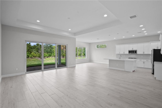 unfurnished living room featuring sink, light hardwood / wood-style flooring, and a raised ceiling