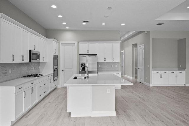 kitchen with white cabinetry, sink, stainless steel appliances, a center island with sink, and light hardwood / wood-style flooring