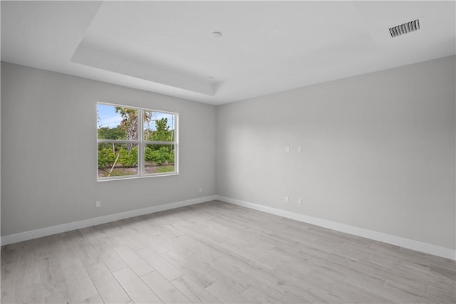 empty room with a raised ceiling and light hardwood / wood-style flooring