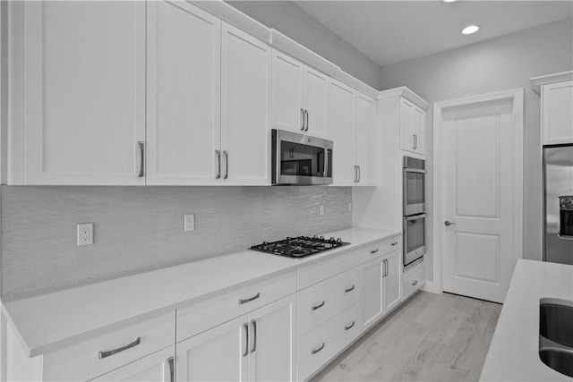 kitchen with white cabinetry, appliances with stainless steel finishes, tasteful backsplash, and light wood-type flooring