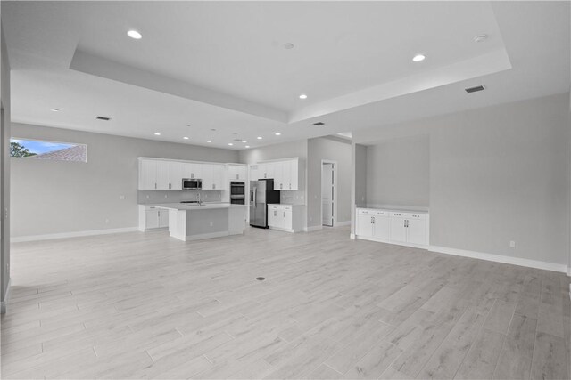 unfurnished living room with a tray ceiling and light wood-type flooring