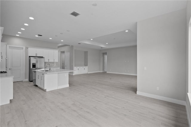 kitchen featuring sink, a kitchen island with sink, white cabinetry, stainless steel fridge with ice dispenser, and decorative backsplash