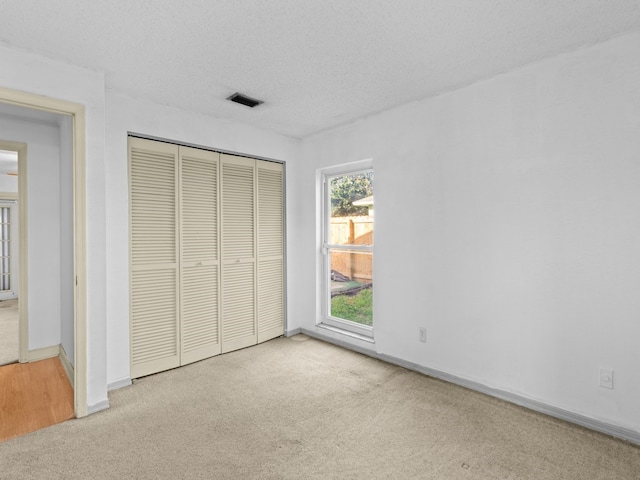 unfurnished bedroom with light colored carpet, a textured ceiling, and a closet