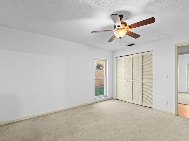 unfurnished bedroom with light carpet, a textured ceiling, a closet, and ceiling fan