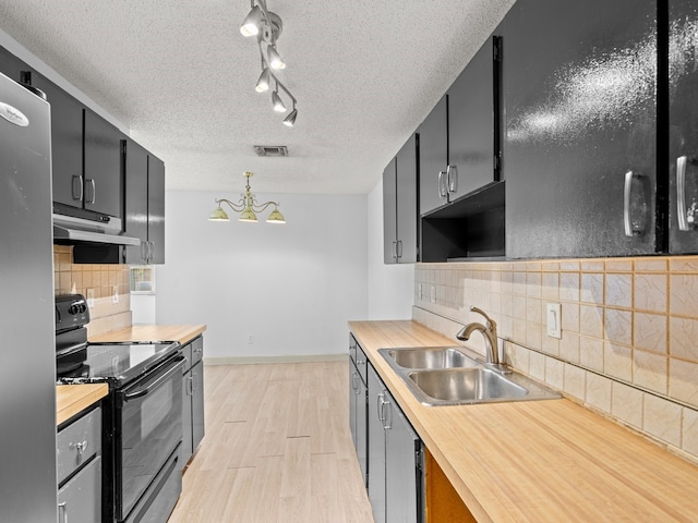 kitchen featuring pendant lighting, wooden counters, black range with electric stovetop, sink, and stainless steel refrigerator