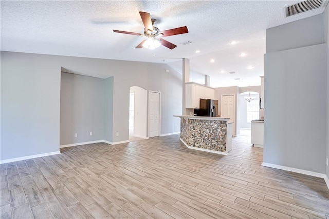 unfurnished living room featuring a textured ceiling, light wood-type flooring, ceiling fan with notable chandelier, and lofted ceiling