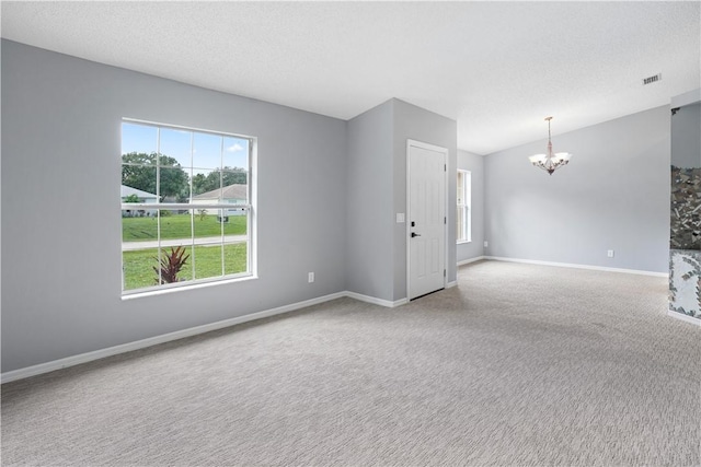 carpeted spare room with a chandelier and a textured ceiling