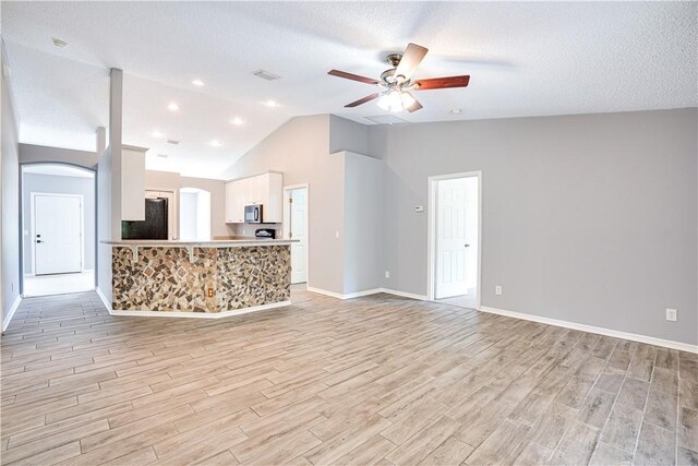 unfurnished living room with ceiling fan, a textured ceiling, and lofted ceiling