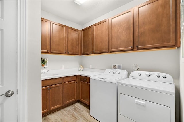 washroom with light wood finished floors, independent washer and dryer, a sink, and cabinet space