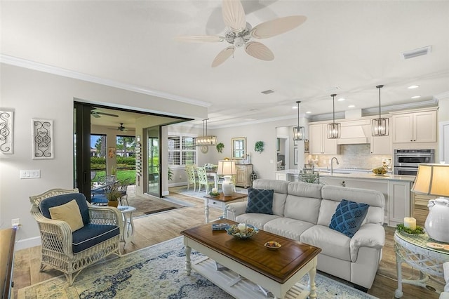 living room with light wood-style flooring, visible vents, baseboards, and ornamental molding