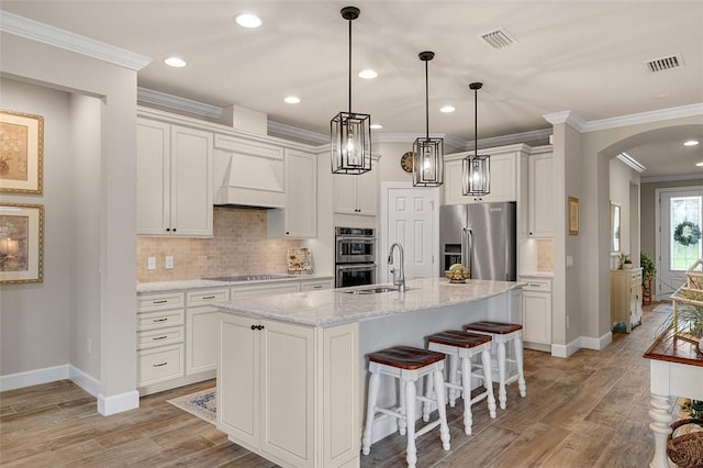 kitchen featuring arched walkways, custom exhaust hood, stainless steel appliances, light wood-style flooring, and ornamental molding