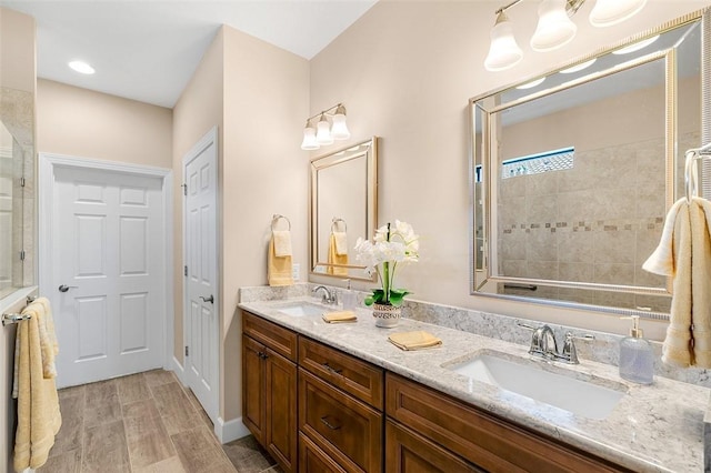 full bathroom with double vanity, wood finished floors, a sink, and tiled shower