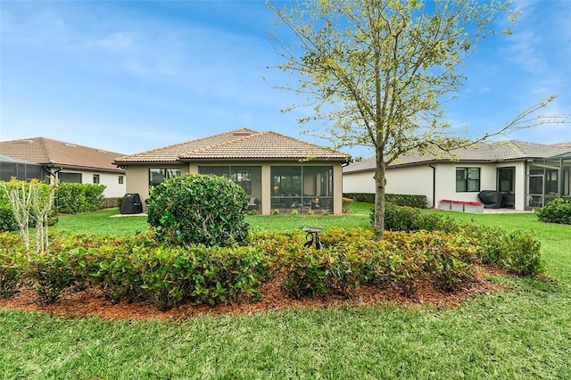 rear view of property with a sunroom, a tile roof, a yard, and stucco siding