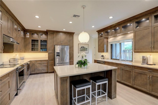 kitchen featuring sink, hanging light fixtures, stainless steel appliances, a kitchen island, and light wood-type flooring