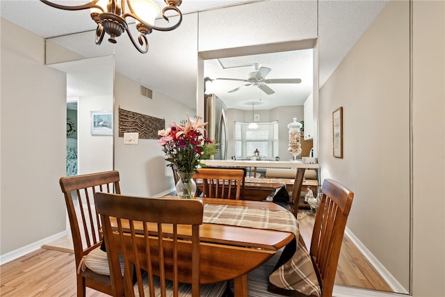 dining room featuring light hardwood / wood-style floors, ceiling fan with notable chandelier, and a textured ceiling