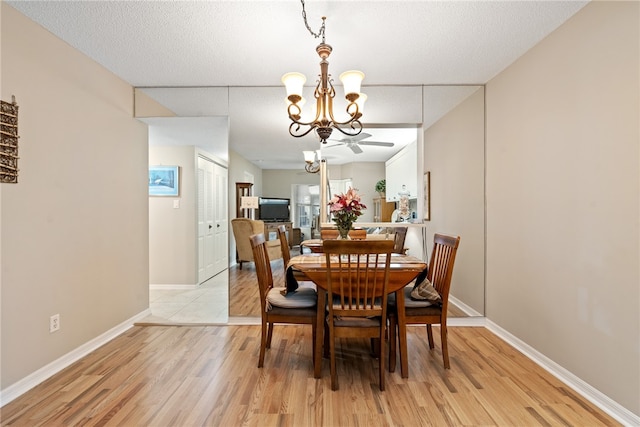 dining room with ceiling fan with notable chandelier, a textured ceiling, and light wood-type flooring