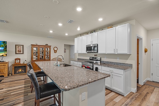 kitchen with white cabinets, a kitchen bar, stainless steel appliances, sink, and a kitchen island with sink