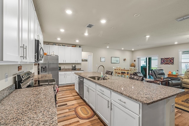 kitchen featuring stainless steel appliances, sink, white cabinets, and an island with sink