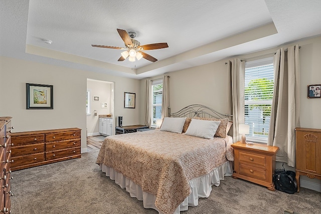 bedroom with ceiling fan, multiple windows, ensuite bathroom, and a raised ceiling