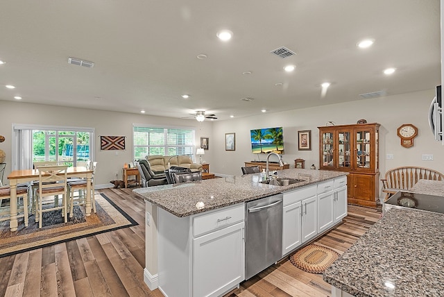 kitchen with light stone countertops, white cabinetry, an island with sink, sink, and stainless steel dishwasher