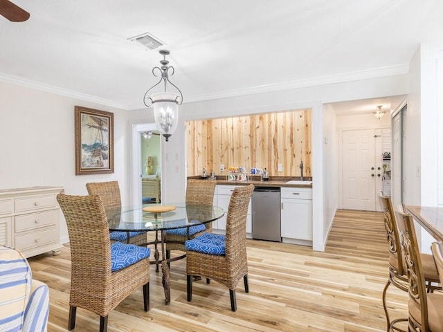 dining room featuring ornamental molding, light wood-type flooring, sink, and an inviting chandelier