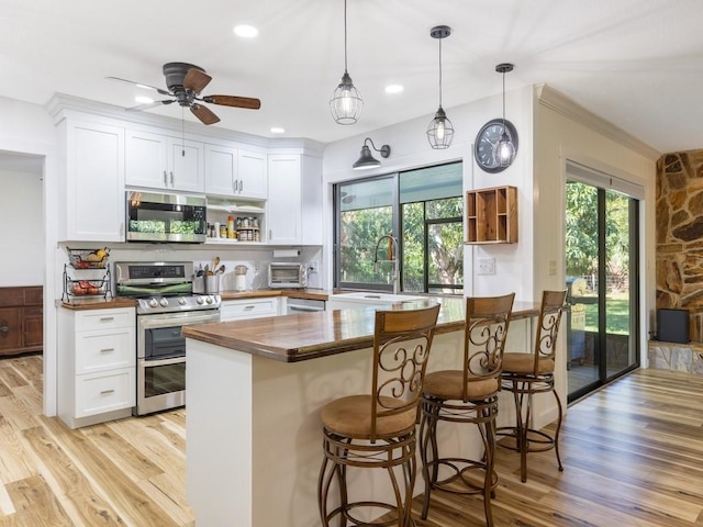 kitchen with appliances with stainless steel finishes, sink, pendant lighting, white cabinetry, and butcher block counters