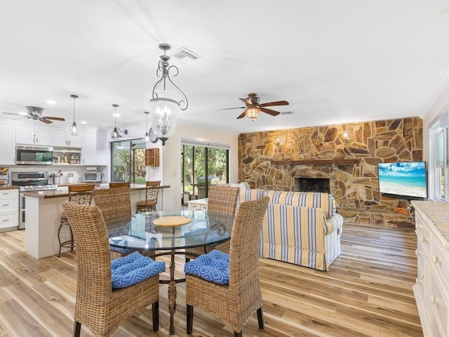 dining room featuring ceiling fan with notable chandelier, light hardwood / wood-style floors, a stone fireplace, and crown molding