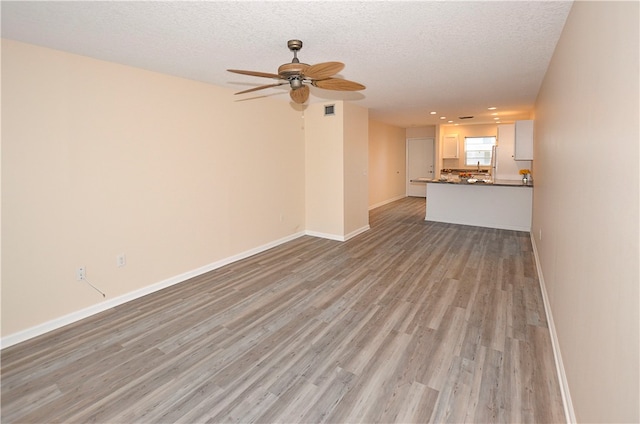 unfurnished living room featuring light wood-type flooring, a textured ceiling, and ceiling fan