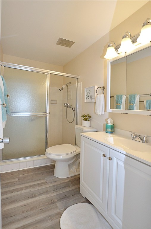 bathroom featuring toilet, vanity, wood-type flooring, and a shower with shower door