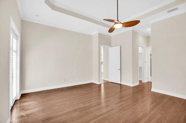 unfurnished bedroom with ornamental molding, a tray ceiling, baseboards, and wood finished floors