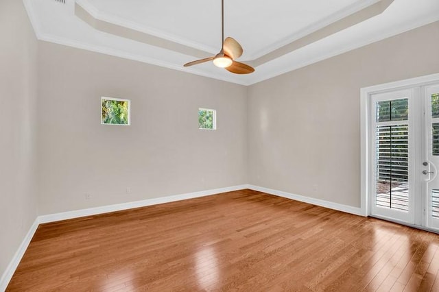 unfurnished room with a wealth of natural light, a tray ceiling, baseboards, and light wood finished floors