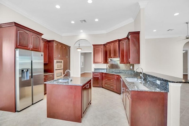 kitchen with dark stone counters, arched walkways, stainless steel fridge, and a sink