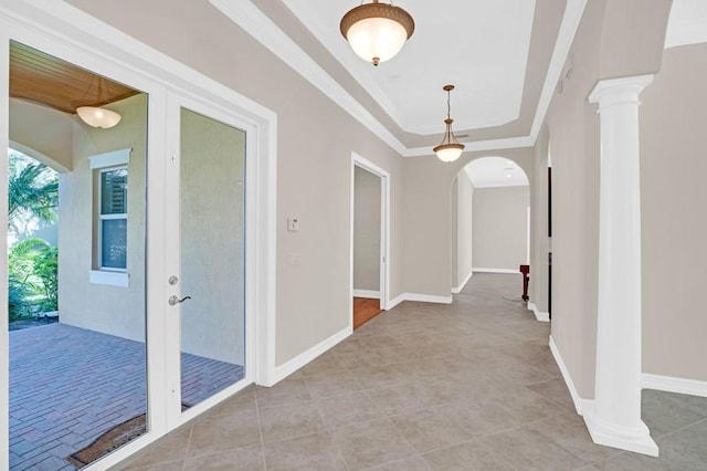 hallway featuring a raised ceiling, arched walkways, crown molding, light tile patterned floors, and baseboards