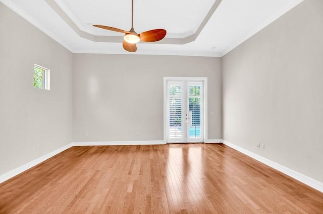 empty room featuring baseboards, a raised ceiling, crown molding, and light wood finished floors