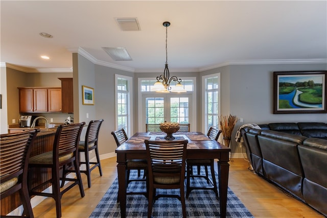 dining area featuring light wood-type flooring, a chandelier, sink, and ornamental molding