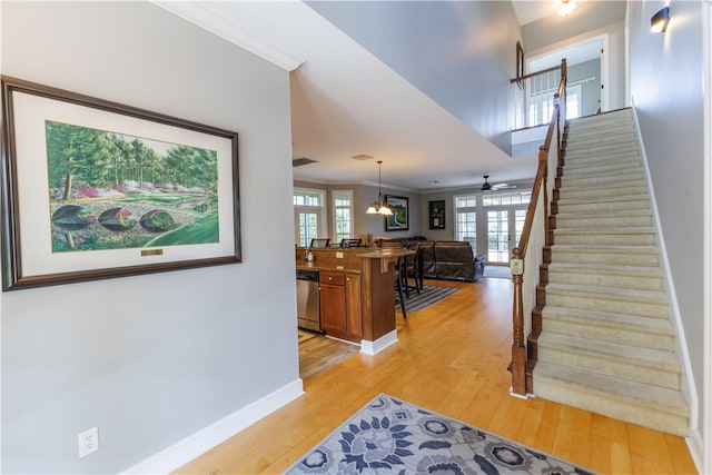 stairs featuring ceiling fan with notable chandelier, wood-type flooring, and crown molding