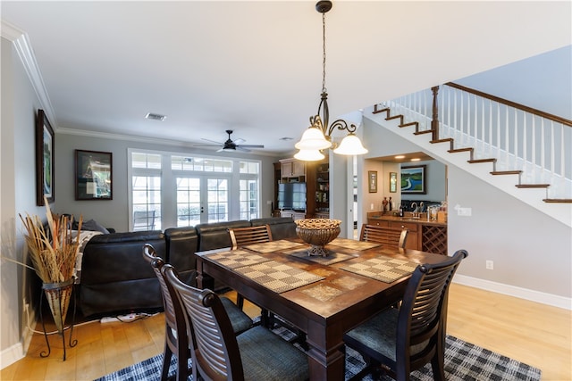 dining room featuring french doors, light wood-type flooring, ceiling fan with notable chandelier, and crown molding