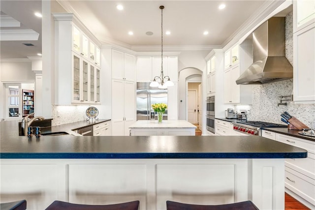 kitchen with pendant lighting, sink, a kitchen breakfast bar, stainless steel appliances, and wall chimney exhaust hood