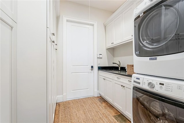 laundry area featuring cabinets, stacked washer / dryer, and sink