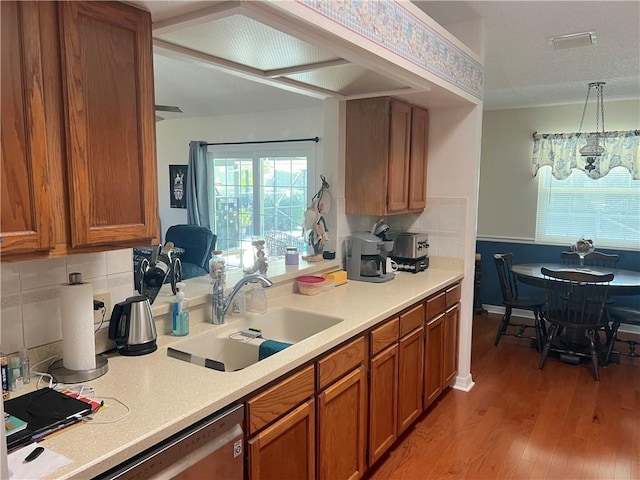 kitchen featuring sink, dishwasher, backsplash, decorative light fixtures, and light wood-type flooring