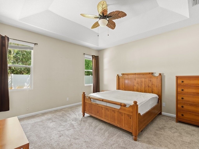 bedroom with a tray ceiling, baseboards, light carpet, and ceiling fan