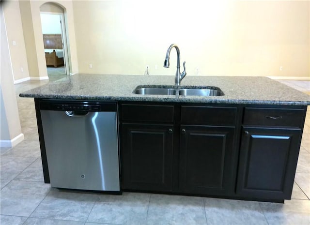 kitchen with arched walkways, a sink, baseboards, stainless steel dishwasher, and light stone countertops